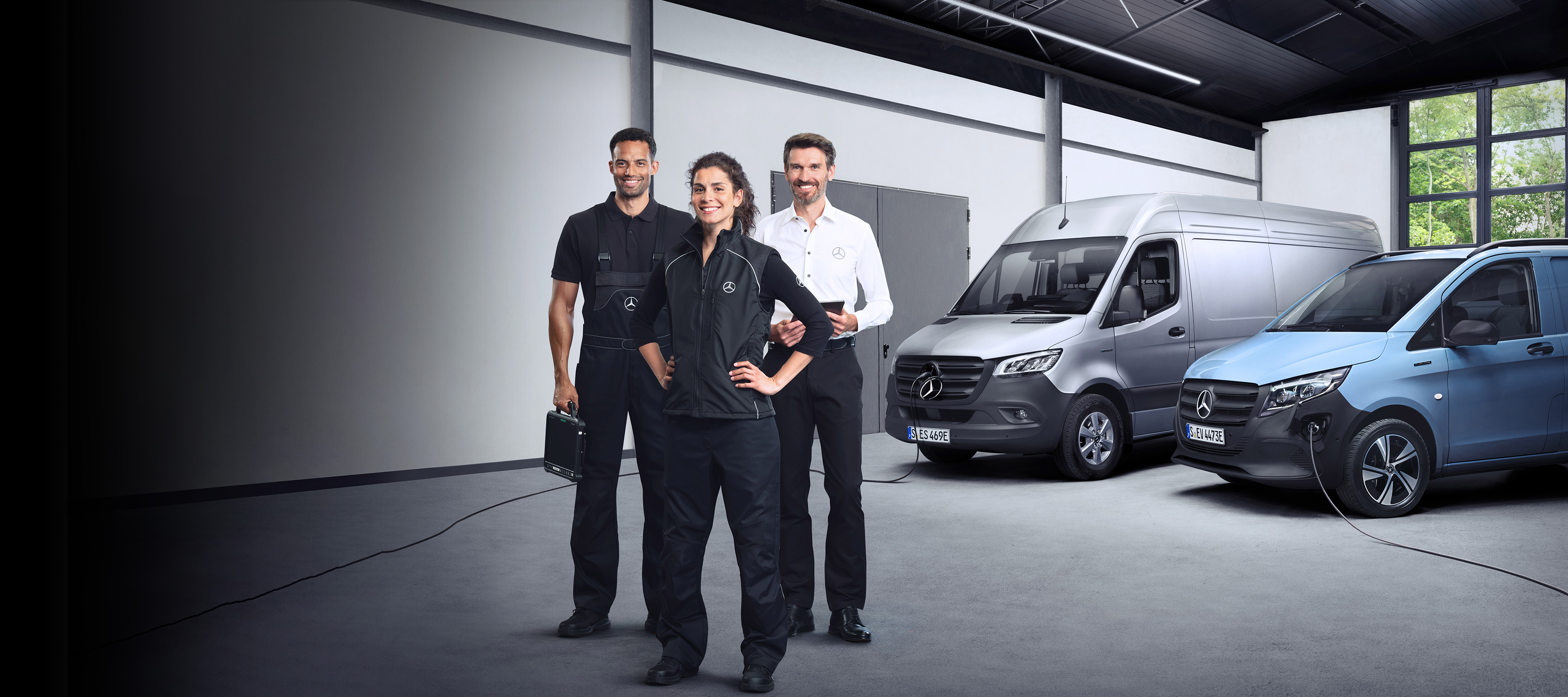 Serwis Mercedes-Benz do elektrycznych samochodów dostawczych. Trzej pracownicy z zespołu serwisowego Mercedes-Benz stoją przed samochodami Mercedes-Benz eSprinter i Mercedes-Benz eVito.
