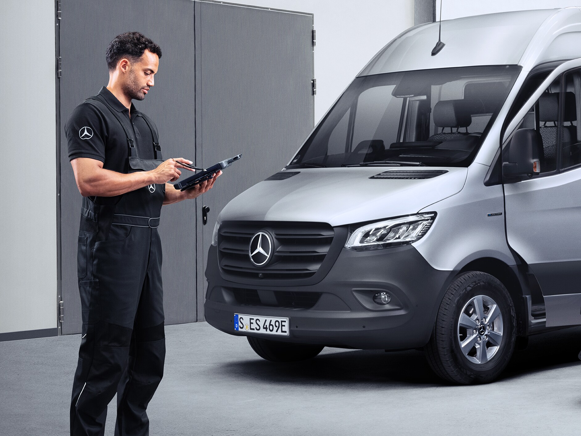 Partner serwisowy Mercedes-Benz patrzy na ekran tabletu, stojąc przed pojazdem Mercedes-Benz eSprinter.