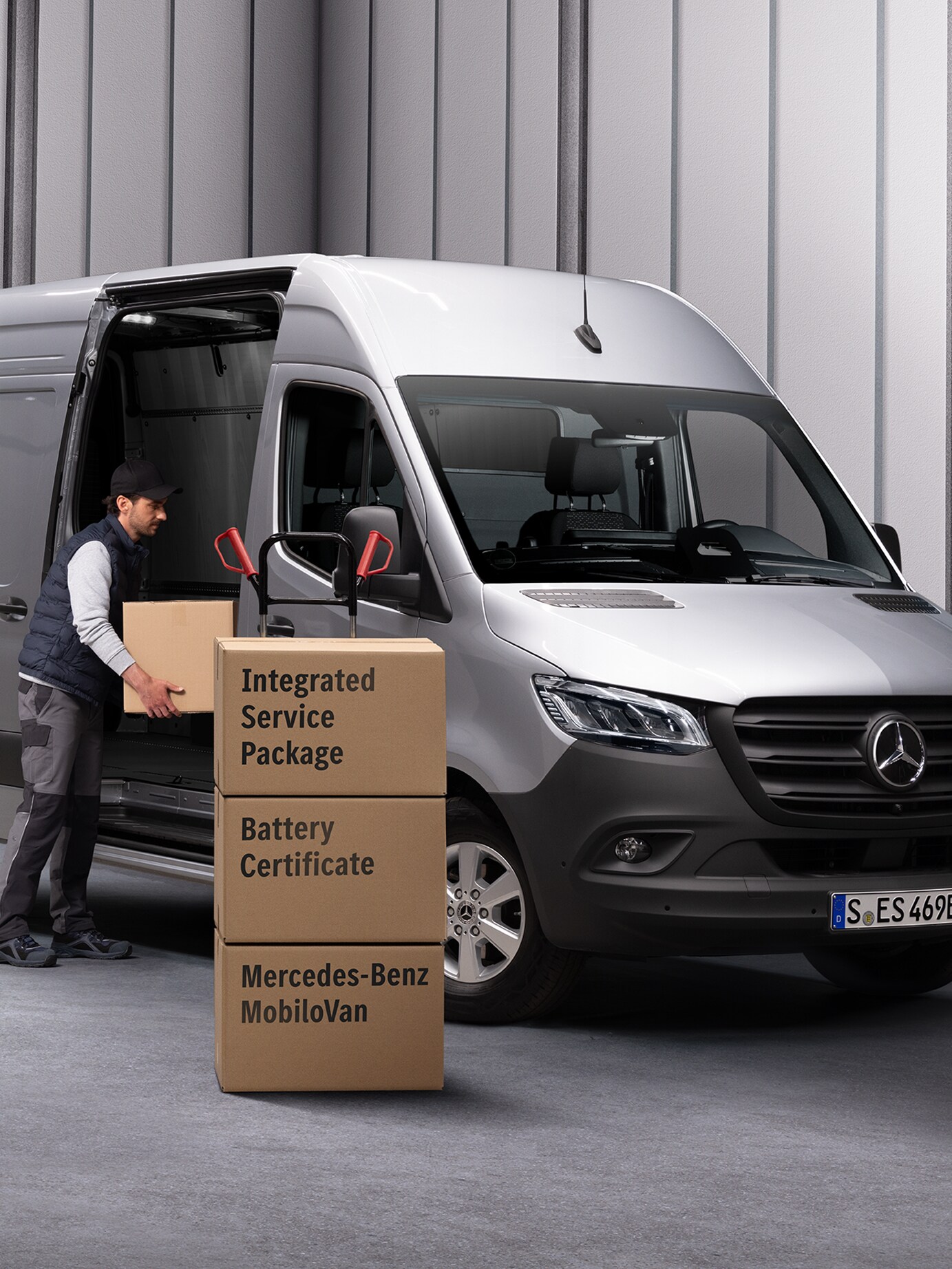 Osoba wyładowuje kartony z pojazdu Mercedes-Benz eSprinter. Trzy kartony ułożone w stos przed samochodem dostawczym. Na kartonach umieszczone są etykiety z nazwami produktów Umów serwisowych Mercedes-Benz.