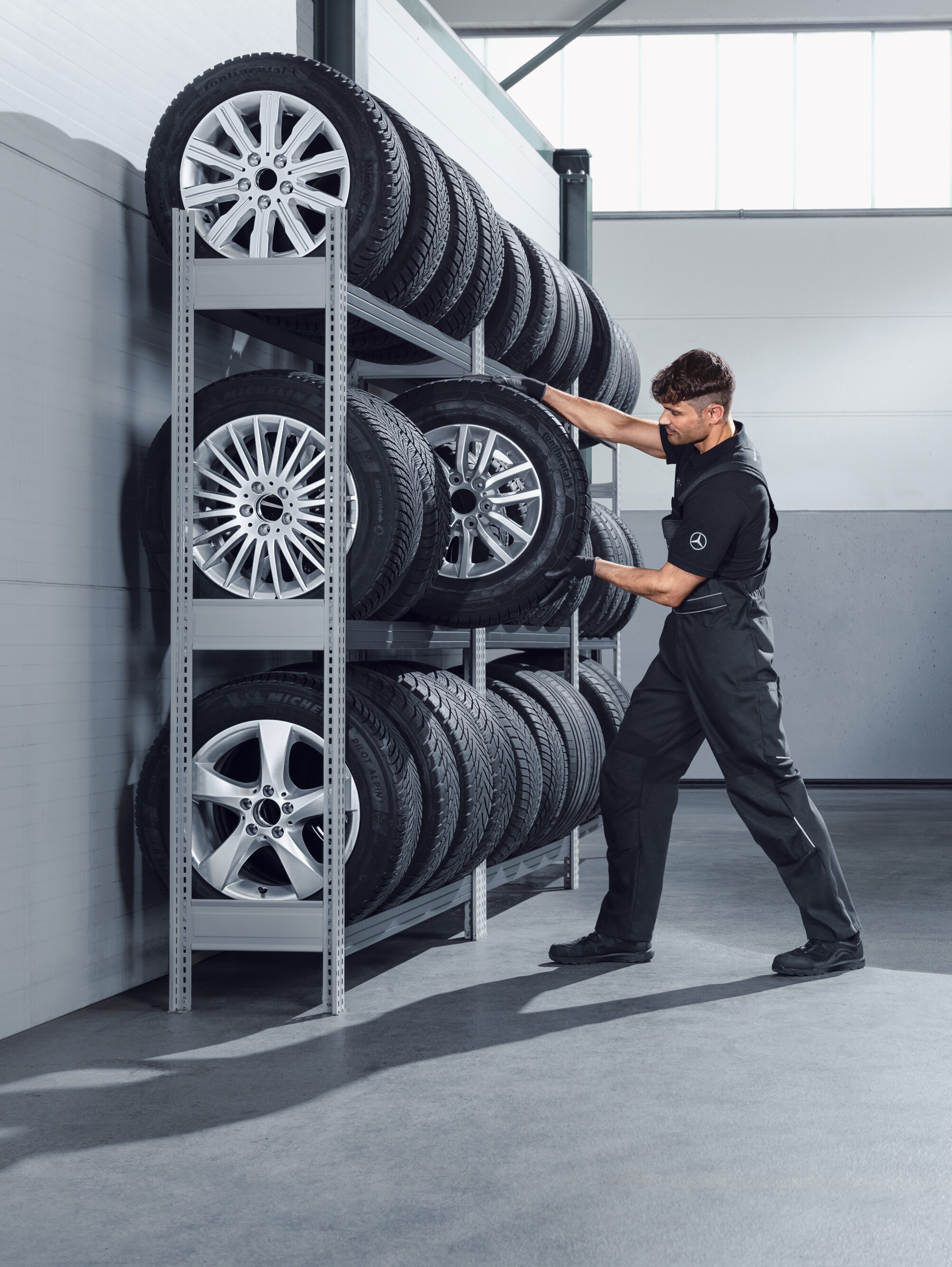 Mechanik wybierający z regału serwisowego kompletne koła zimowe Mercedes-Benz do białego samochodu Sprinter.