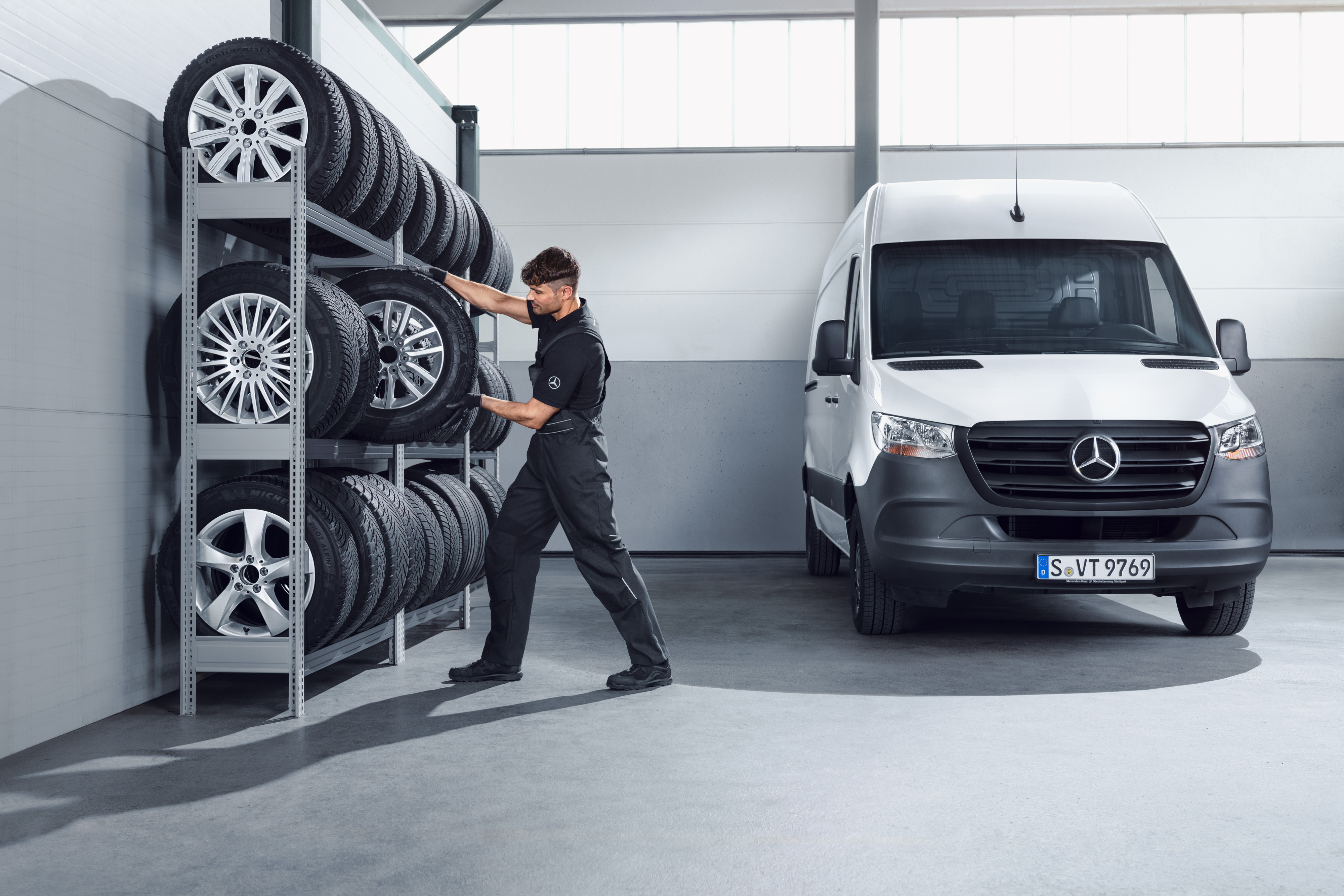 Mercedes-Benz | Wysokiej jakości Oryginalne Części Mechanik wybierający z regału serwisowego kompletne koła zimowe Mercedes-Benz do białego samochodu Sprinter.