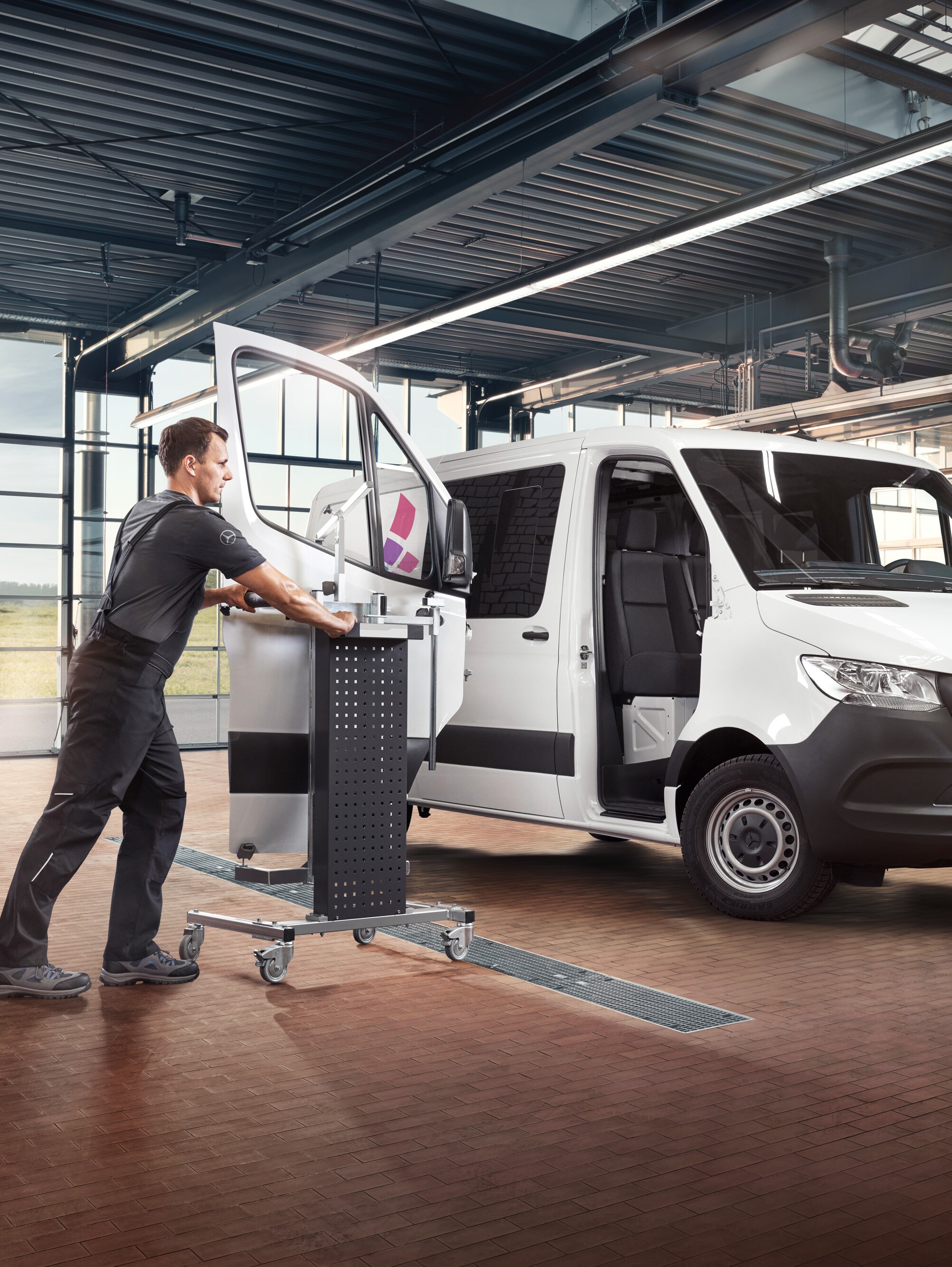 Technik wykonuje serwis drzwi od strony pasażera w białym samochodzie dostawczym Mercedes-Benz Sprinter.