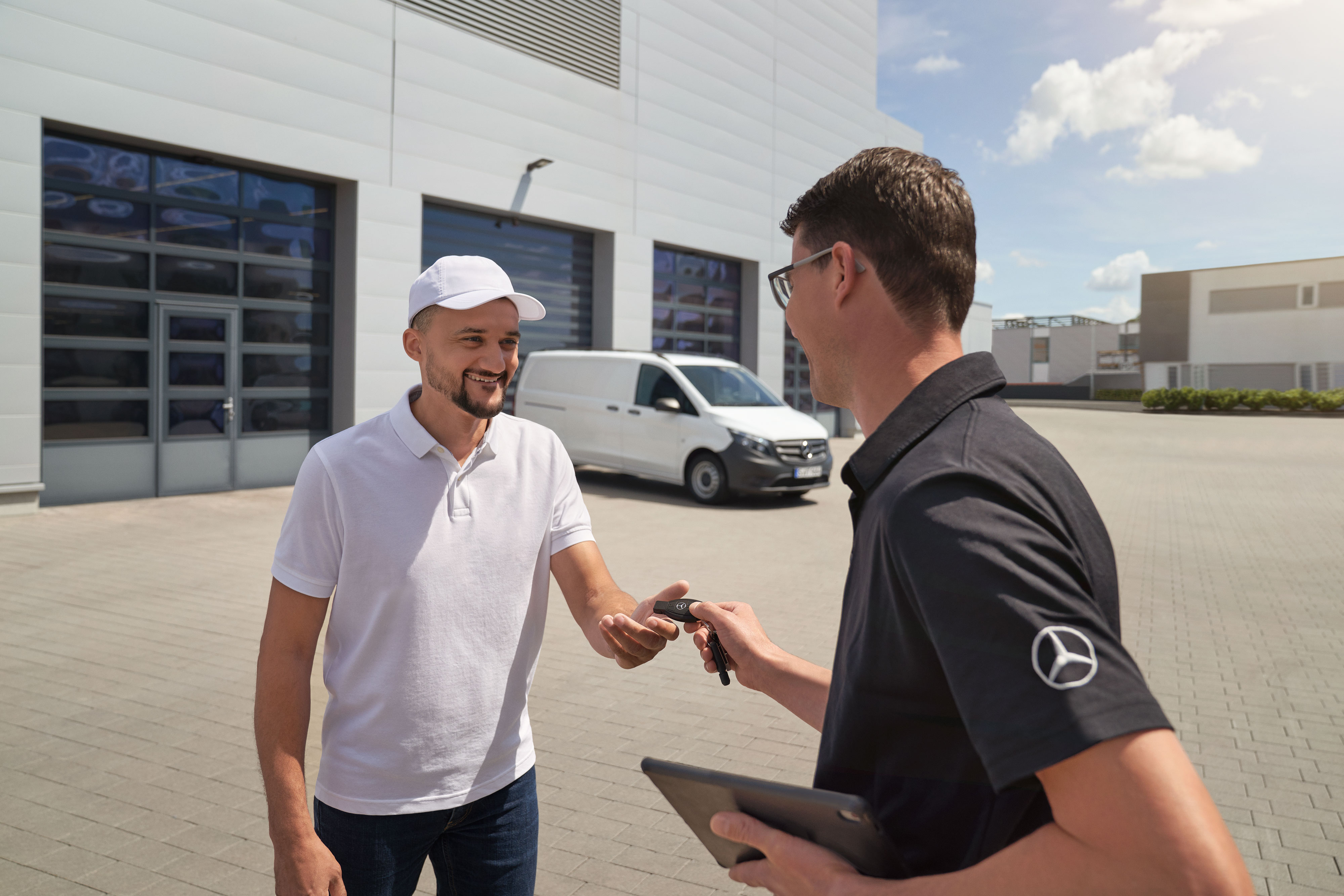 Mercedes-Benz | Serwisowanie | Odbiór i dowóz Przedstawiciel serwisu Mercedes-Benz przekazuje klientowi kluczyki, z białym samochodem dostawczym Mercedes-Benz Vito w tle.