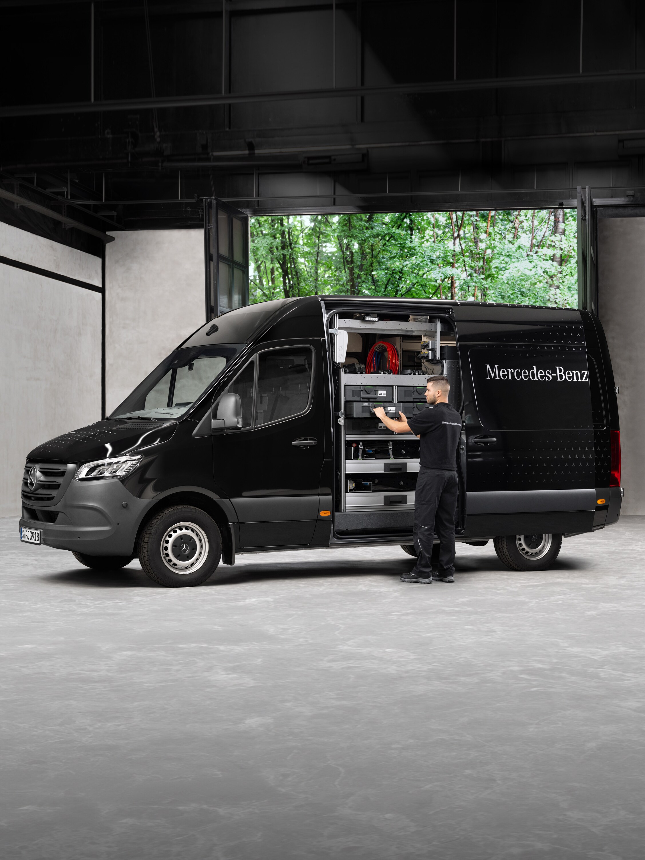 Technik wyjmuje narzędzia z czarnego samochodu dostawczego Mercedes-Benz Sprinter.