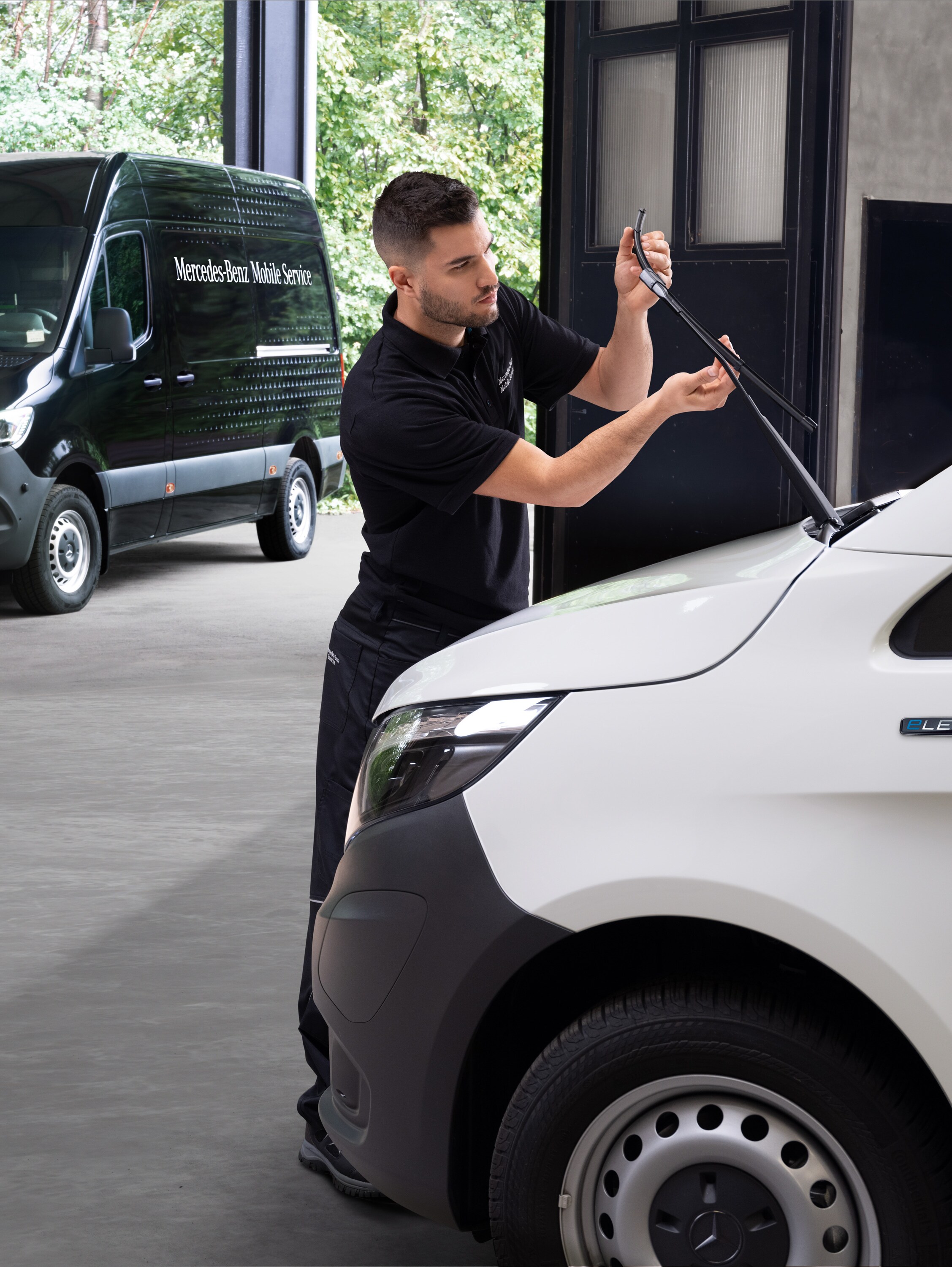 Technik wymienia wycieraczki w białym samochodzie dostawczym Mercedes-Benz Vito.