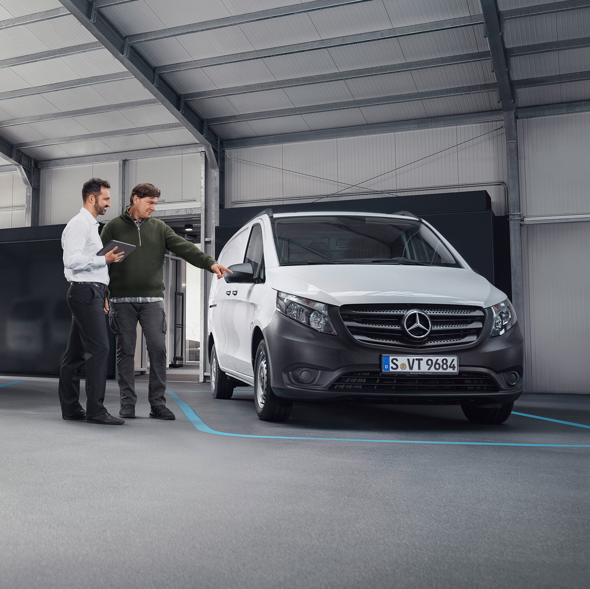 Przedstawiciel obsługi klienta Mercedes-Benz z klientem w zakładzie partnera serwisowego, przed samochodem dostawczym.