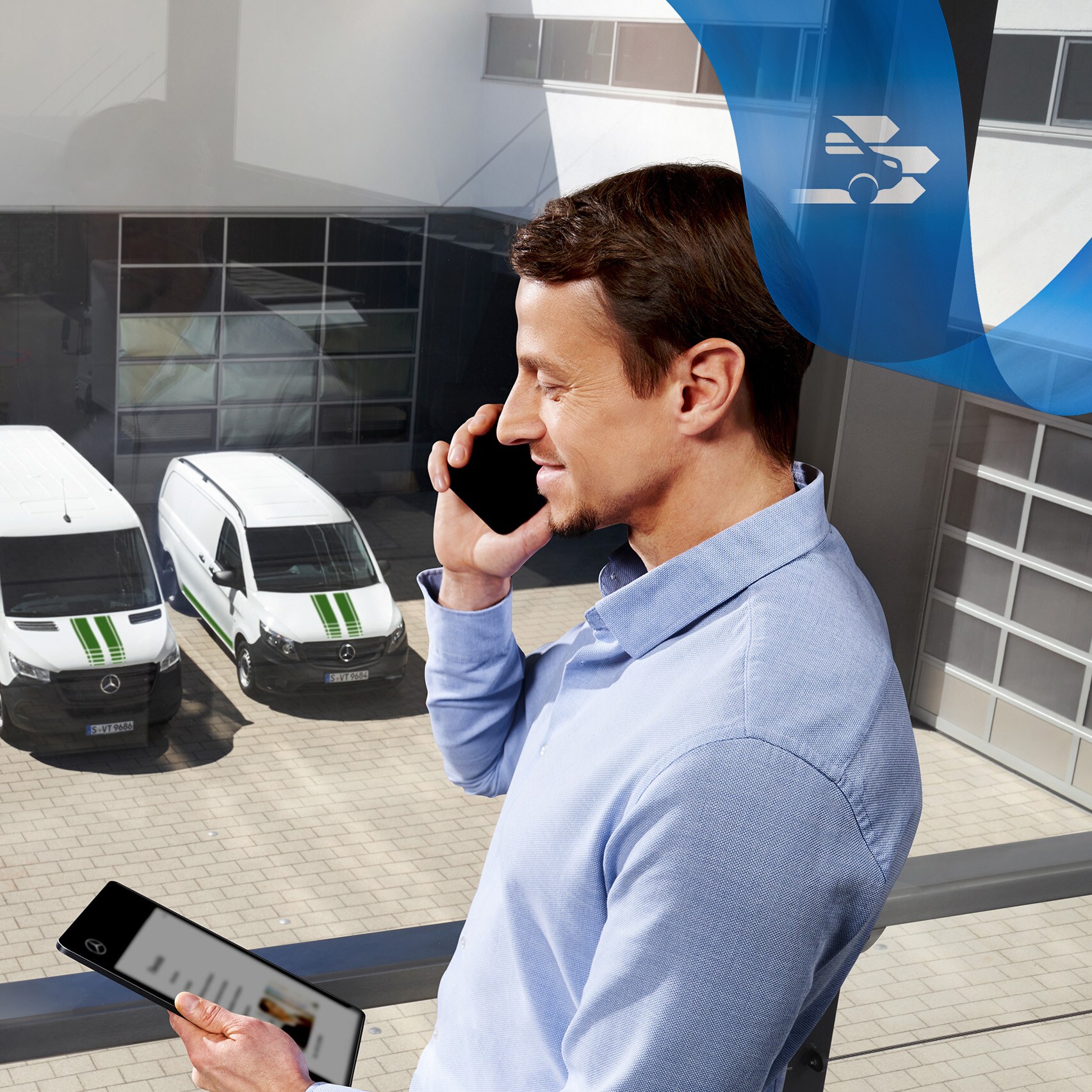 Mężczyzna rozmawia przez telefon komórkowy, pracując na tablecie, w tle szereg samochodów dostawczych Mercedes-Benz.