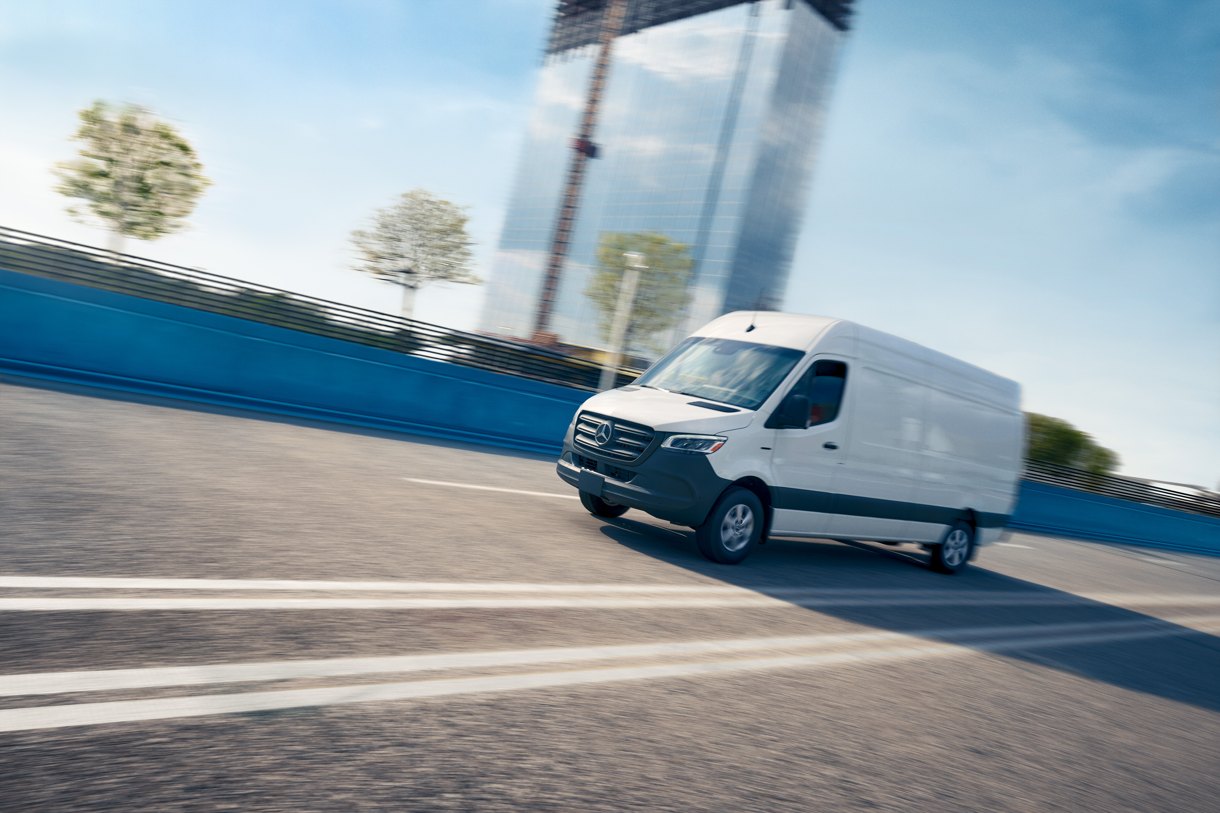 Mercedes-Benz | Technologia samochodów dostawczych | Pokładowa aplikacja Service Biały samochód dostawczy jadący drogą, reklamujący aplikację serwisową Mercedes-Benz umożliwiającą rezerwację wizyt online.