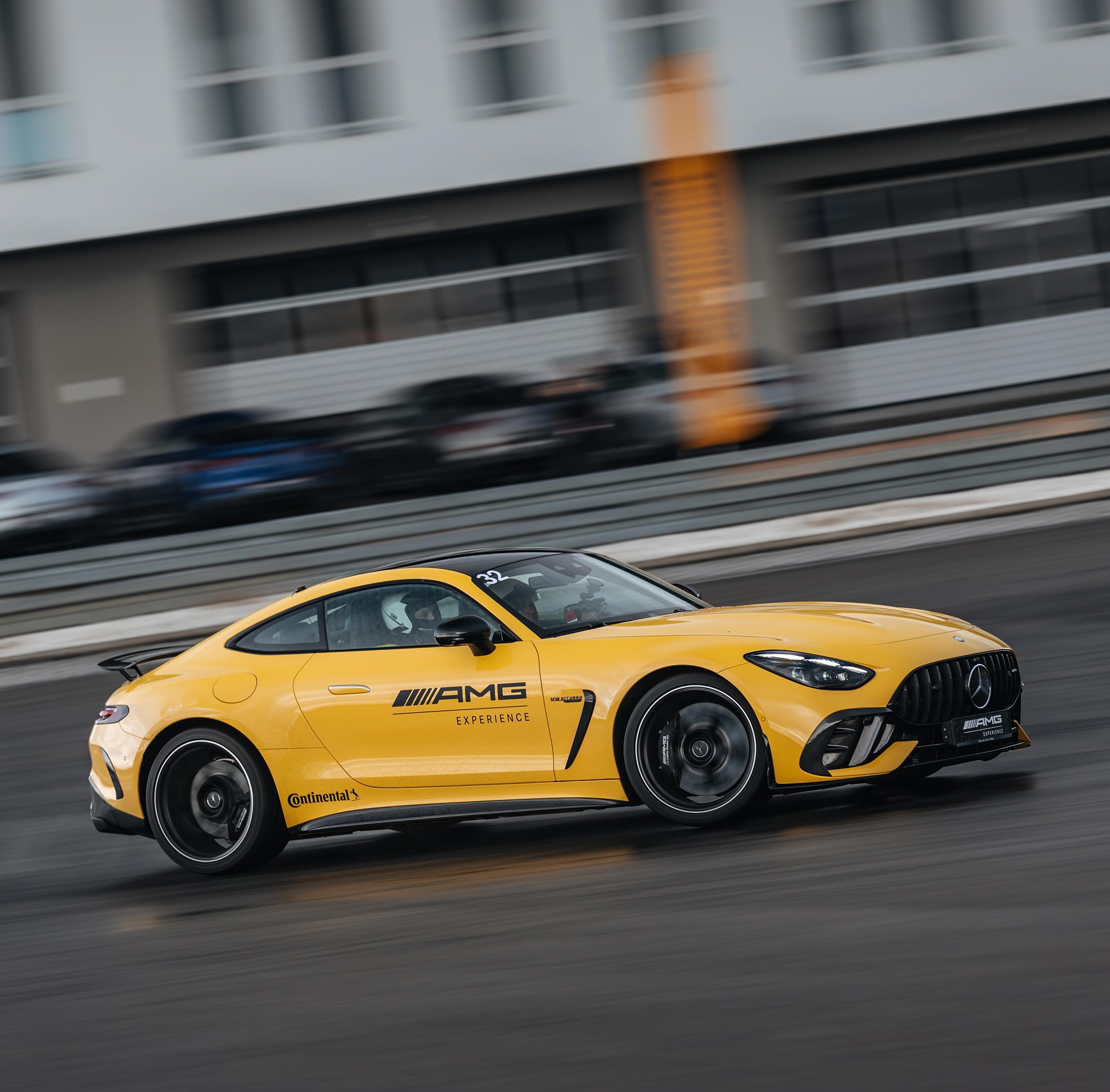 Żółty Mercedes-AMG GT Coupé z logo AMG Experience na drzwiach jedzie na torze wyściegowym.