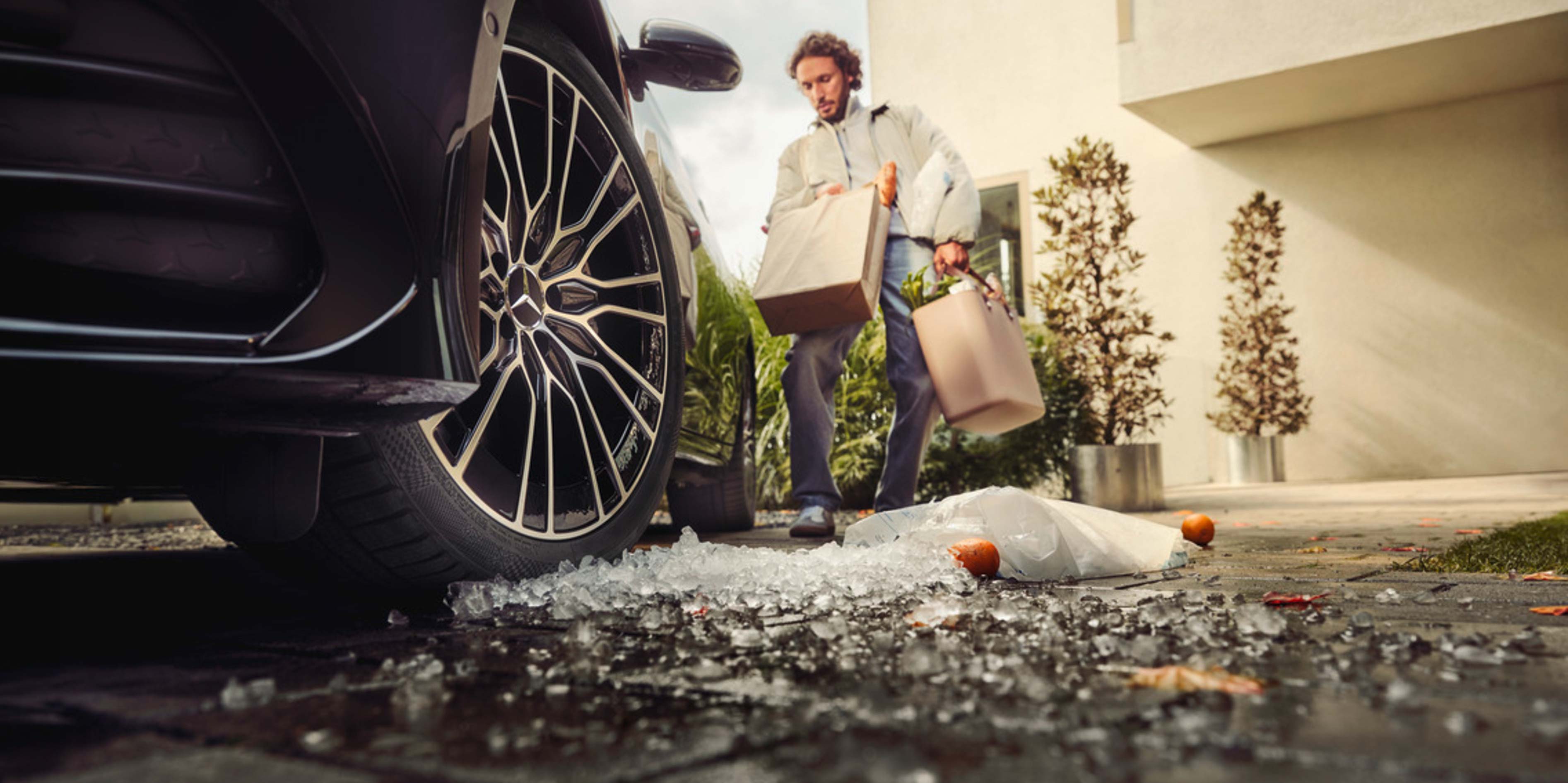 Opony zimowe | Mercedes-Benz Koło czarnego Mercedesa z rozsypanymi wokół kostkami lodu.