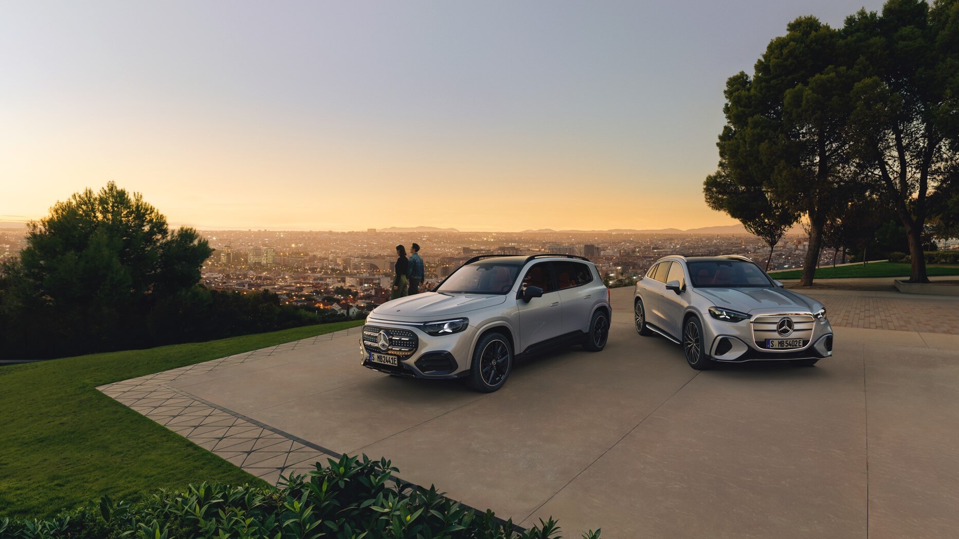 Srebrne modele GLB i GLC zaparkowane na tle zachodzącego słońca.