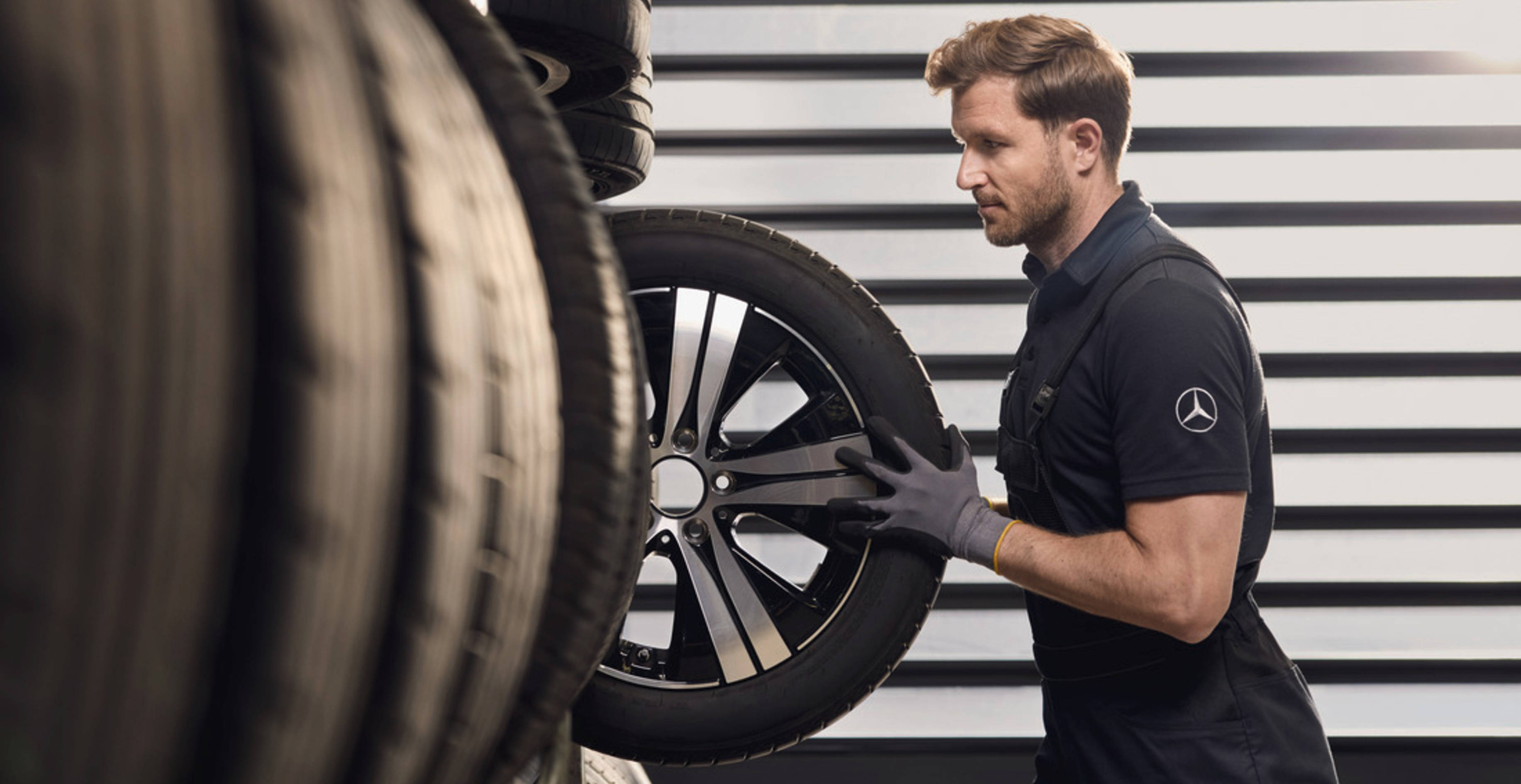 Zmień opony na zimowe | Mercedes-Benz Pracownik serwisu Mercedes-Benz zdejmuje z regału koło do Mercedesa.