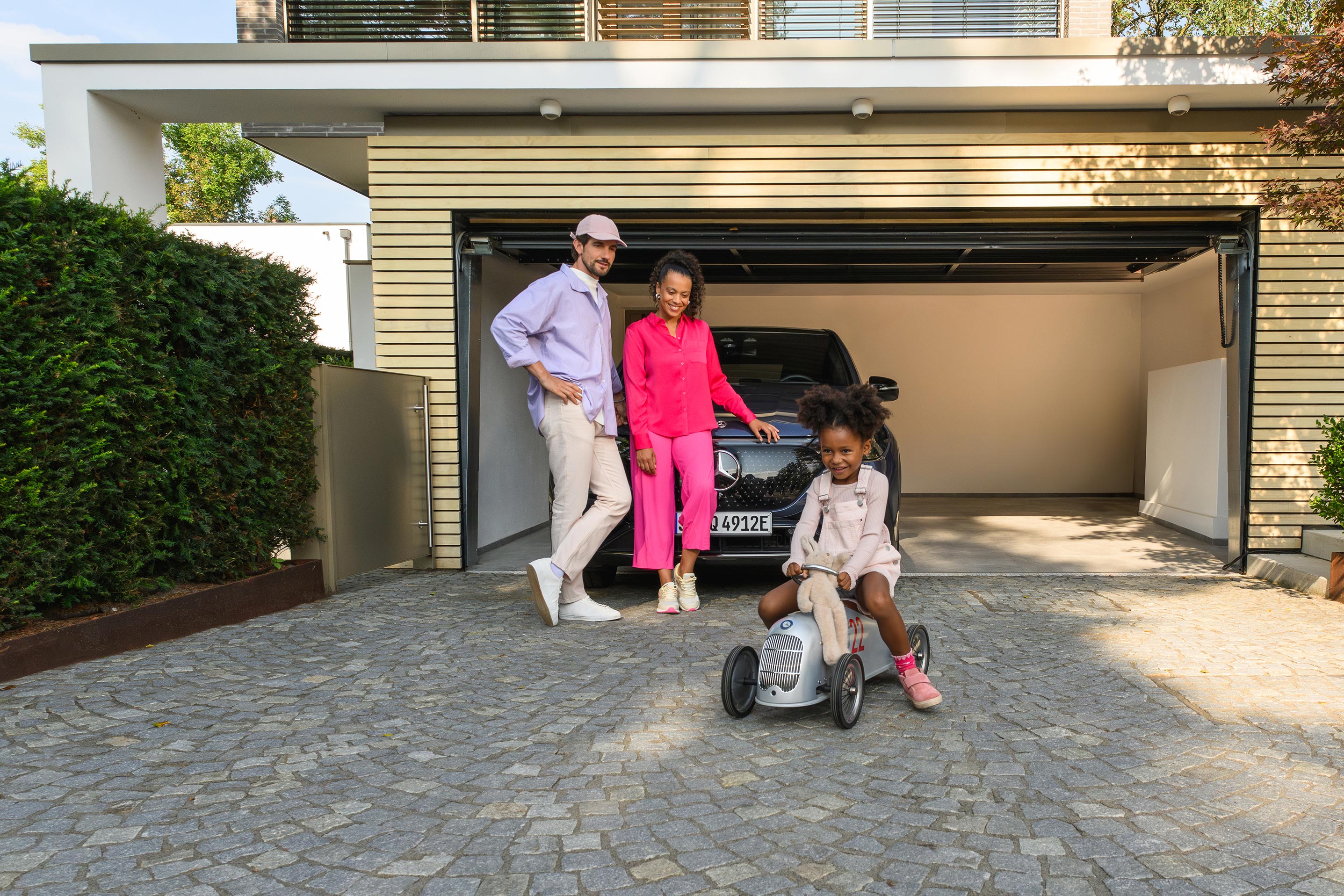 Mercedes‑Benz Financial Services Uśmiechnięta rodzina stojąca przed zaparkowanym modelem Mercedes-Benz.