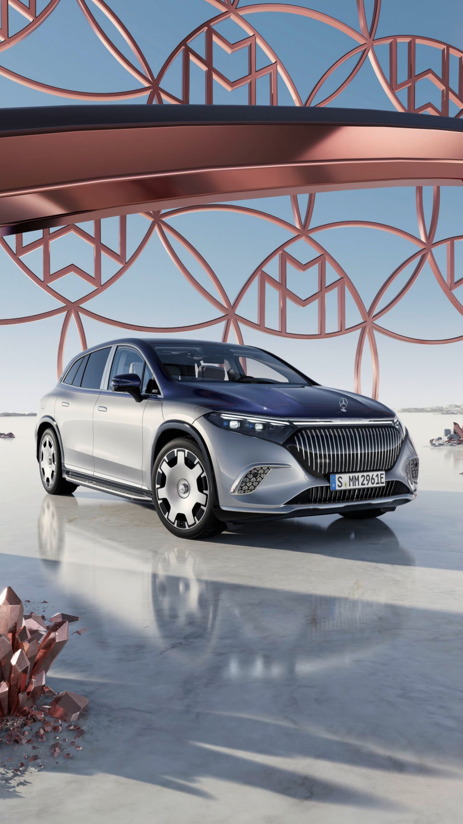 Srebrny Mercedes-Maybach EQS SUV na tle ażurowej konstrukcji z wzorem Mercedes-Maybach.