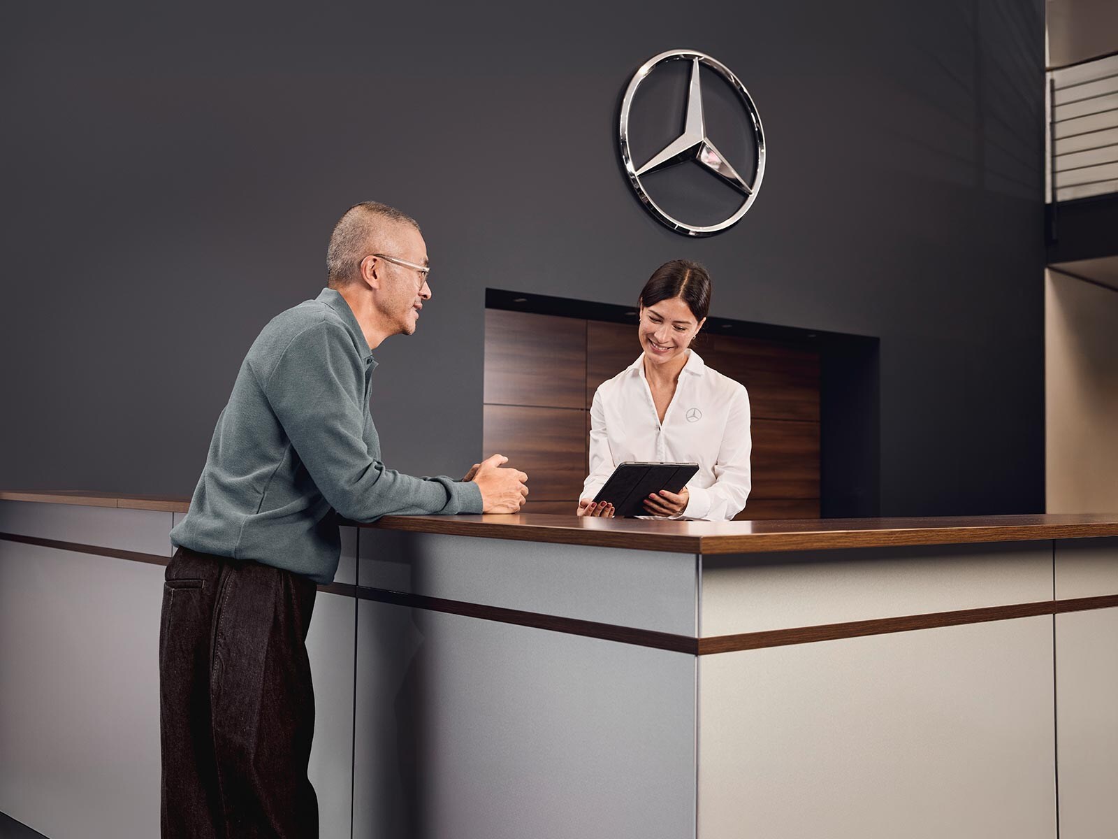 Klient omawia szczegóły serwisu pojazdu z doradcą przy ladzie recepcji w salonie Mercedes-Benz.