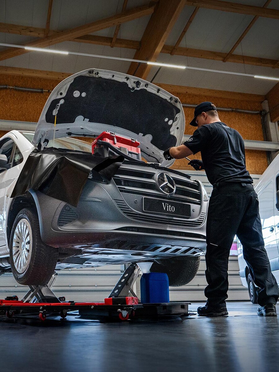 Pracownik serwisu przeprowadza naprawę białego Mercedesa Vito.