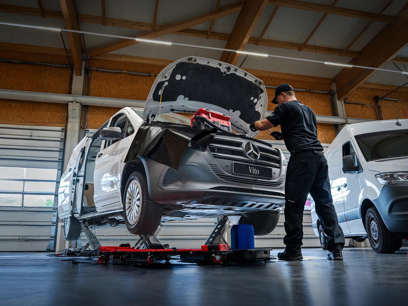 Pracownik serwisu przeprowadza naprawę białego Mercedesa Vito.