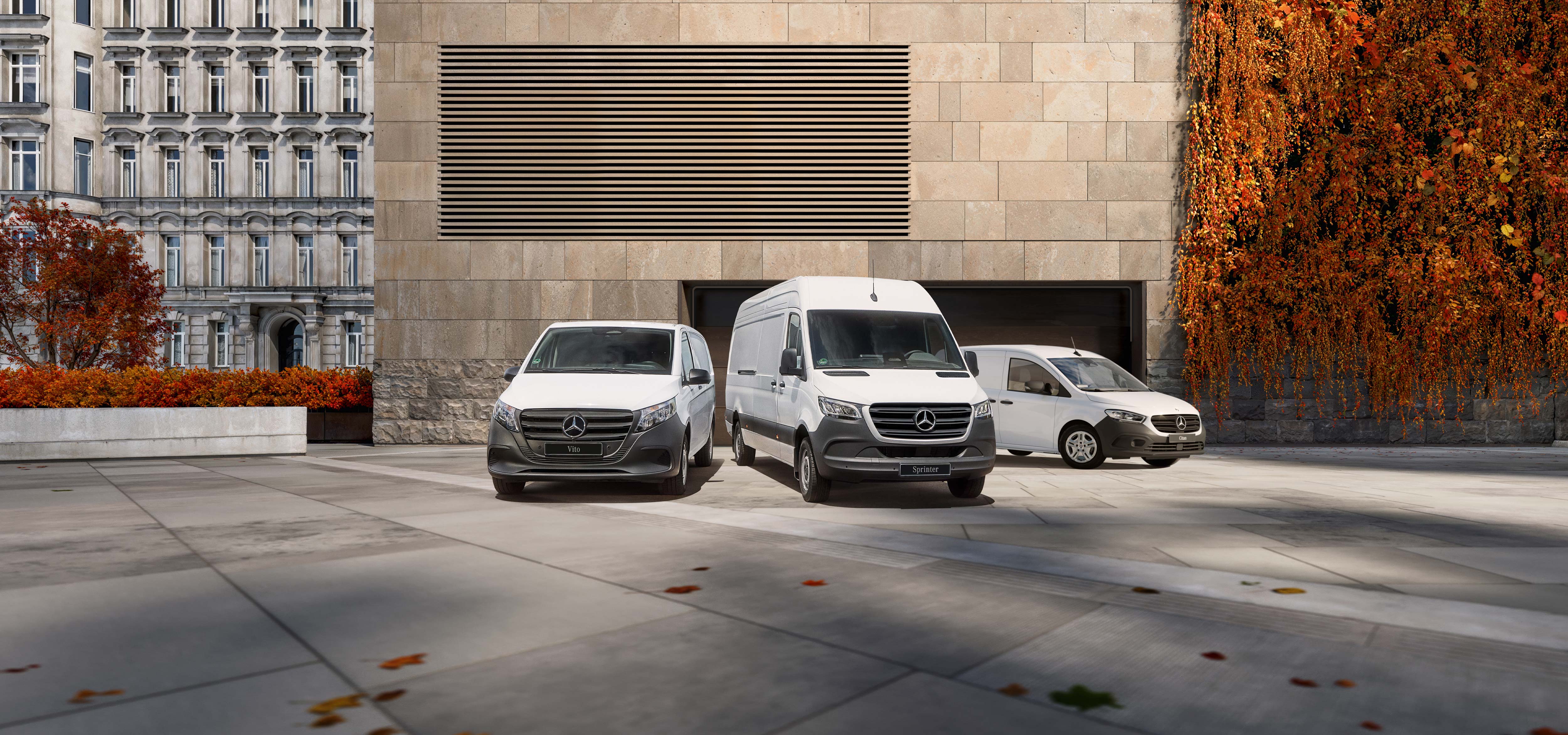 Jesienna wyprzedaż w Mercedes‑Benz | Samochody dostawcze Mercedes-Benz Modele Citan, Vito i Sprinter stoją zaparkowane przed nowoczesnym budynkiem w jesiennej scenerii.