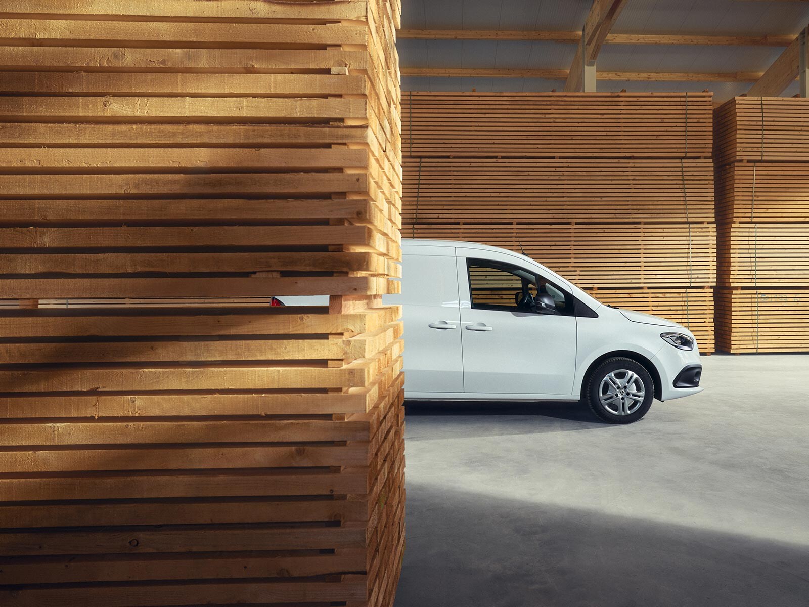 Biały Citan Mercedes-Benz zaparkowany pomiędzy deskami na terenie tartaku.