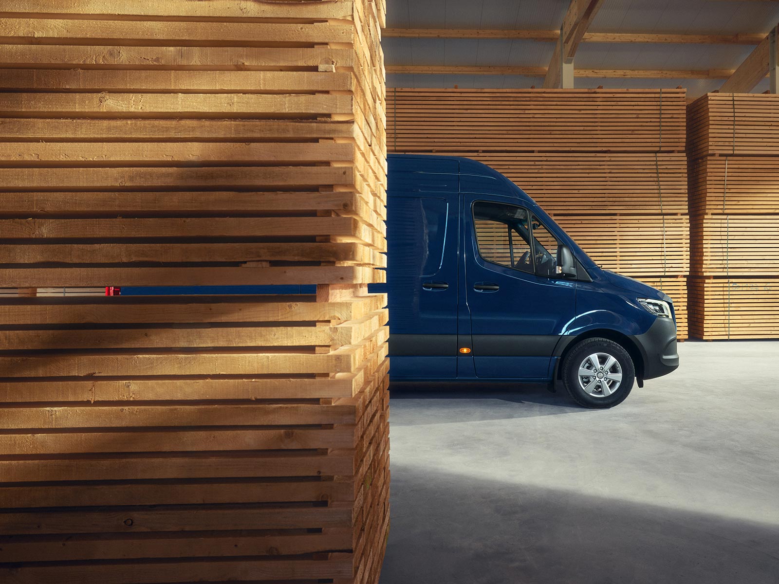 Mercedes-Benz Sprinter Granatowy Sprinter Mercedes-Benz zaparkowany pomiędzy deskami na terenie tartaku.