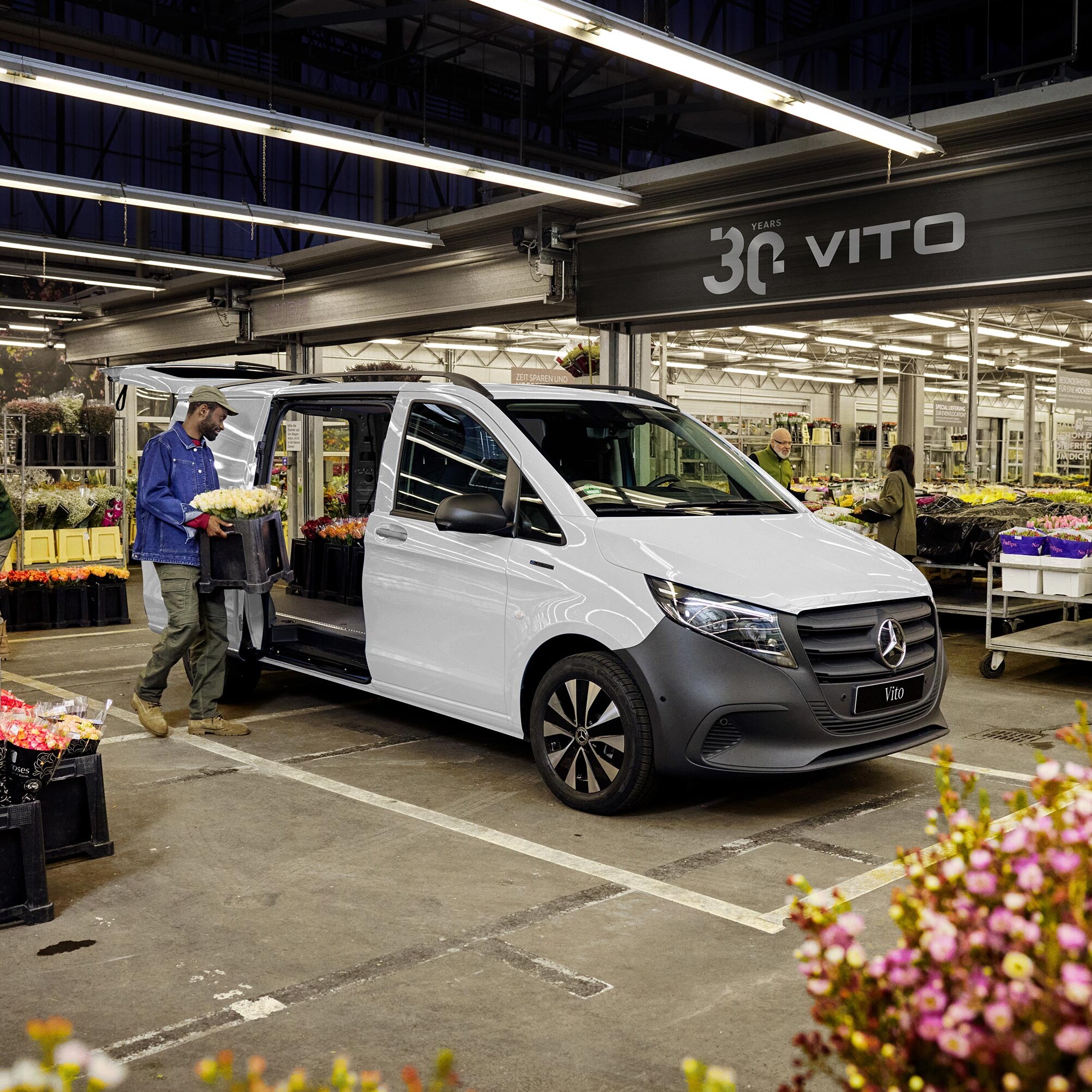 Biały Mercedes-Benz Vito podczas załadunku pojemników z kwiatami.