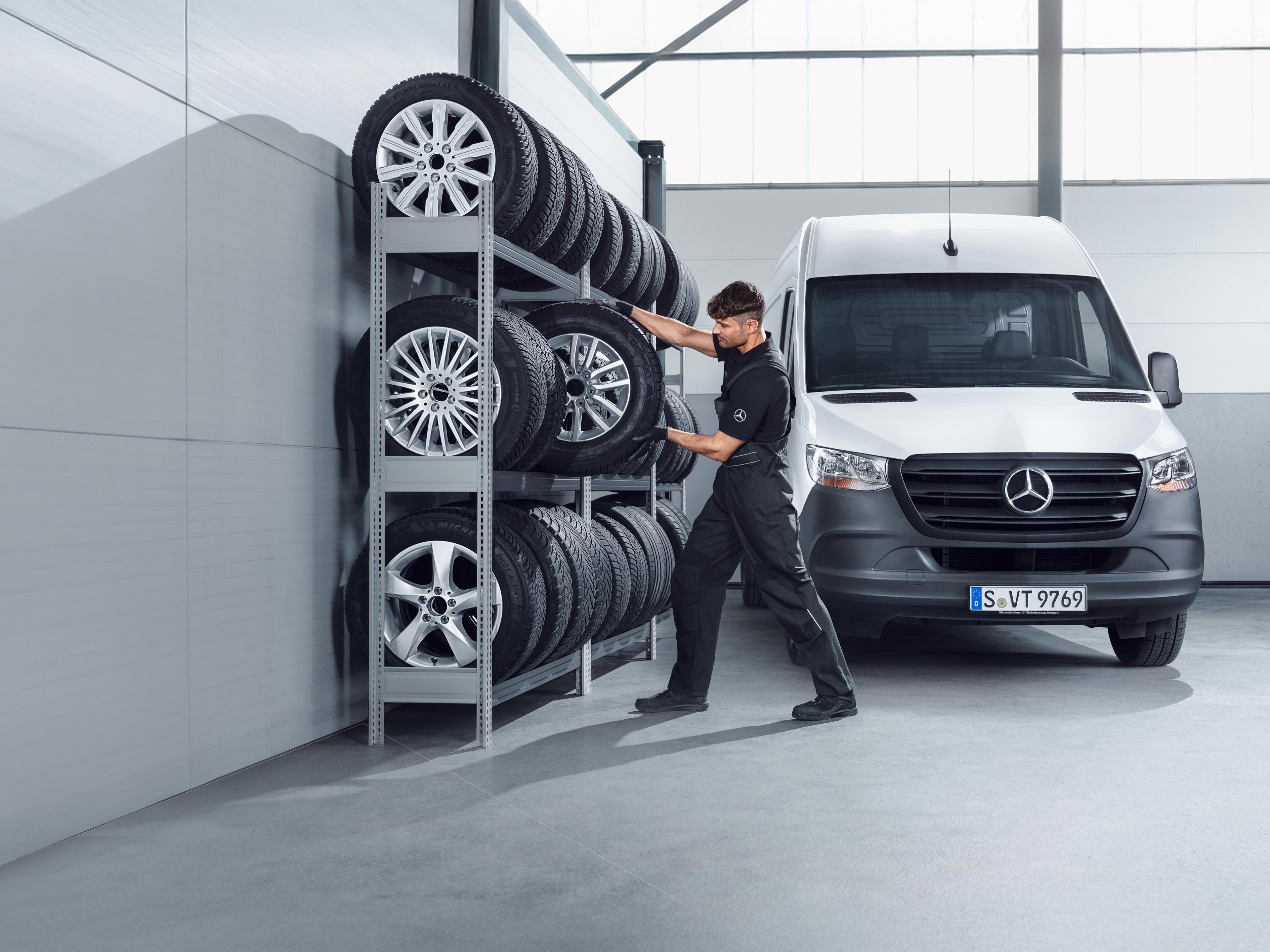 Pracownik serwisu Mercedes-Benz wymienia opony w białym Sprinterze.