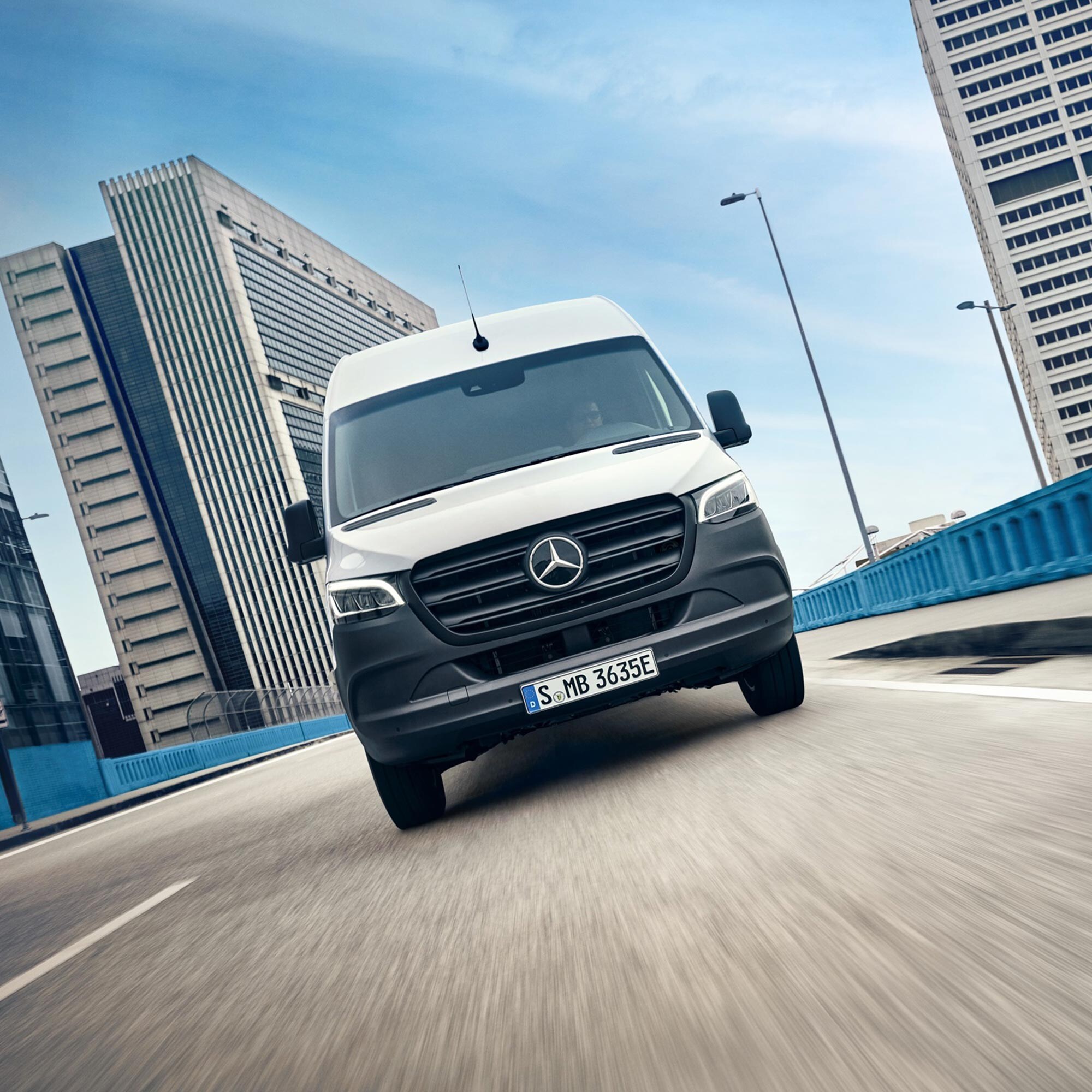 Biały MErcedes eSprinter na drodze wśród budynków biurowych.