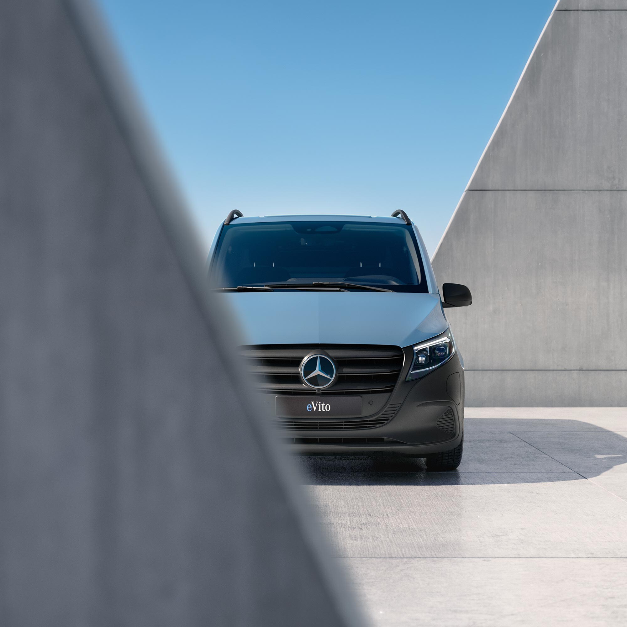 Błękitny Mercedes eVito zaparkowany pomiędzy betonowymi ścianami.