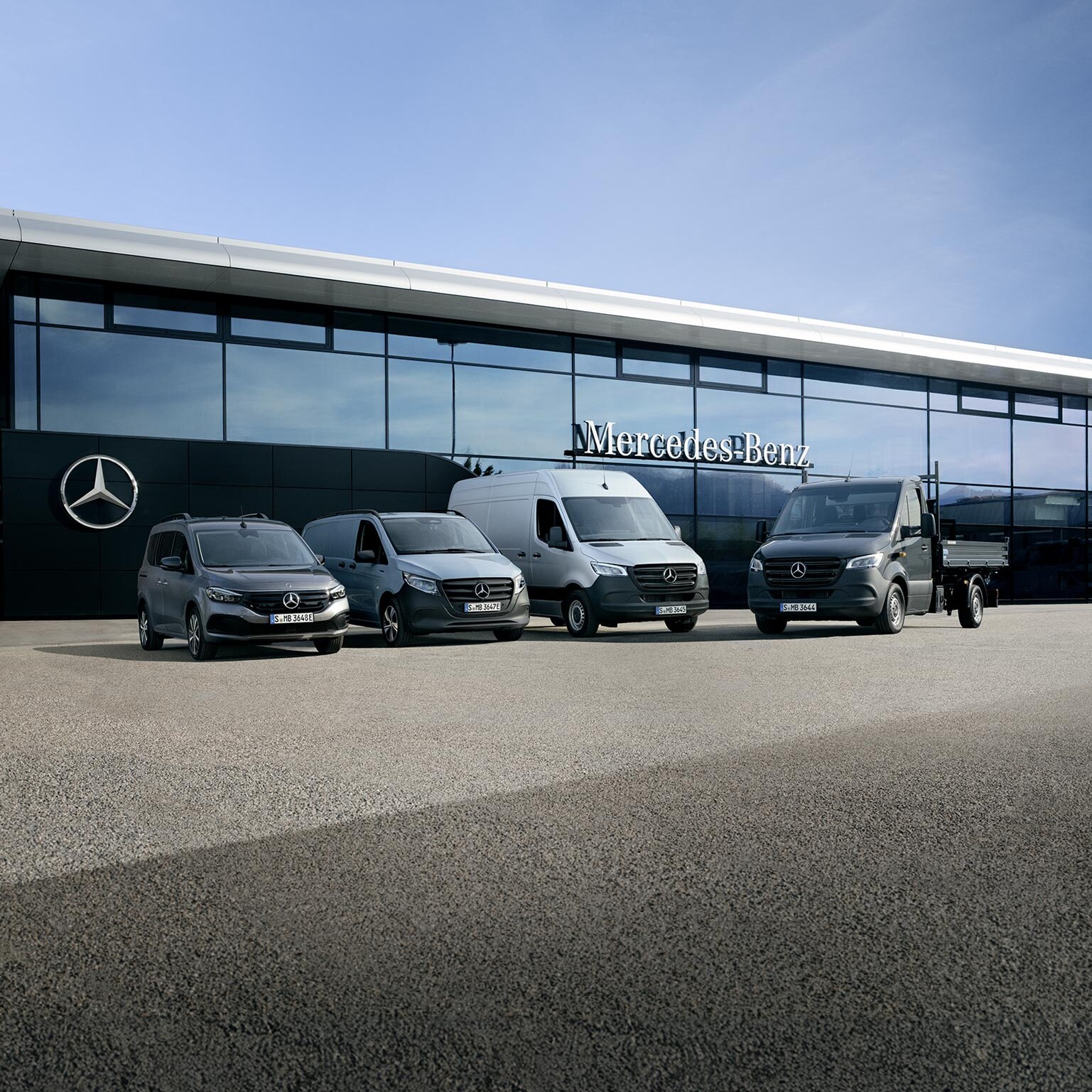 Cztery samochody dostawcze Mercedes-Benz przed budynkiem z logo Mercedes-Benz na szklanej elewacji.