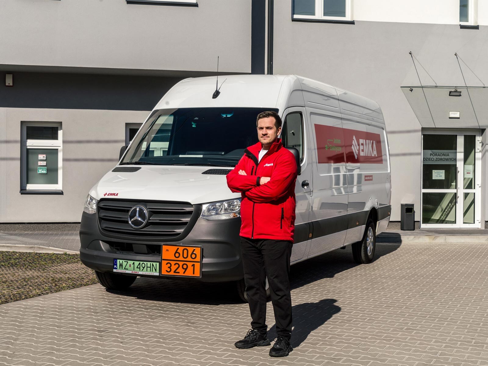 Mężczyzna w czerwonej bluzie stoi przed białym Mercedesem eSprinter.