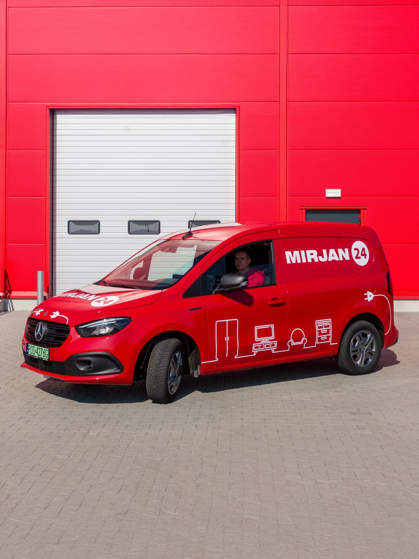 Czerwony eCitany Mercedes-Benz zaparkowany przed budynkiem magazynowym.