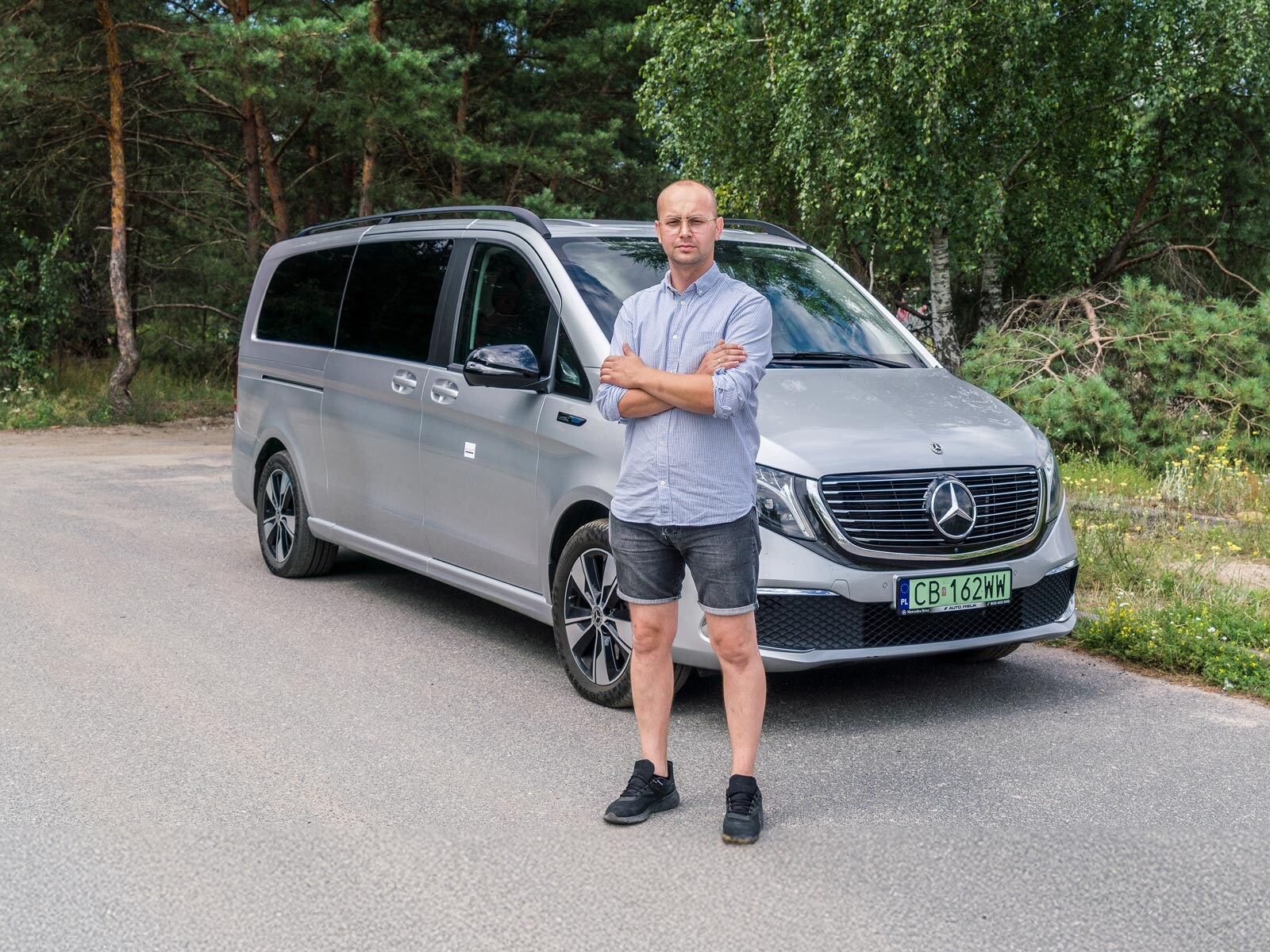 Mężczyzna z założonymi rękami stoi przed srebrnym Mercedesem EQV.