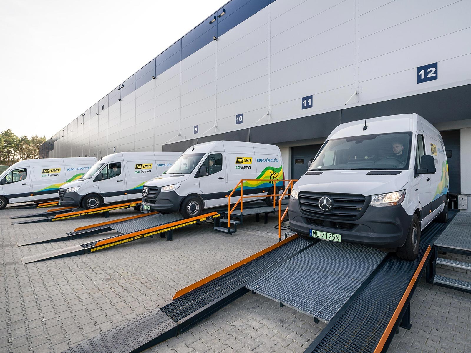 Cztery białe Mercedesy eSprinter na rampie przed magazynem firmy No Limit.
